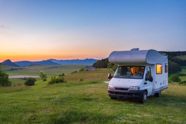 Sunset clear sky over camper van in Montelago highlands, Marche, Italy. Traveling road trip in unique hills and mountains landscape, alternative vanlife vacation concept.