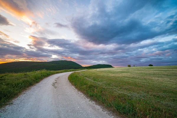 Sunset dramatic sky over country road in Marche region, Italy. Epic clouds above winding trail unique hills and mountains landscape, emotional feeling concept.