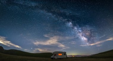 Campo Imperatore dağları üzerinde panoramik gece gökyüzü, Abruzzo, İtalya. Samanyolu galaksisi kavisi ve aydınlatılmış karavanın üzerindeki yıldızlar. Eşsiz tepelerde kamp yapma özgürlüğü.