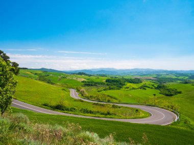 İtalya, Toskana, Volterra Vadisi 'ndeki eşsiz yeşil manzara. Manzaralı dramatik gökyüzü ve gün batımı, ekili tepe sıraları ve tahıl tarlaları, kıvrımlı yol boyunca ağaçlar üzerinde..
