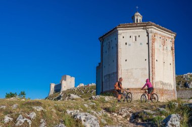 Rocca Calascio 'daki dağların tepesindeki MTB' ye giden adam ve kadın İtalya 'nın Gran Sasso Ulusal Parkı, Abruzzo, İtalya. Açık mavi gökyüzü