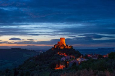 Rocca d 'Orcia, İtalya' nın Toskana şehrinde bir ortaçağ köyü ve kalesi. Alacakaranlıkta eşsiz bir manzara, taş kule dramatik gökyüzüne karşı kayalıklarda tünemişti..