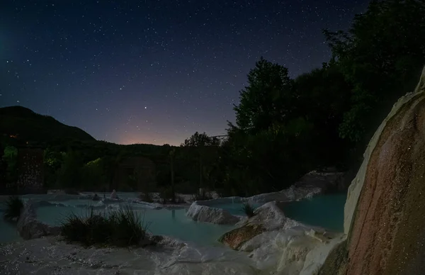 Night view: geothermal pool and hot spring in Tuscany, Italy. Bagni San Filippo natural thermal waterfall in the evening by moon light and stars in the sky.