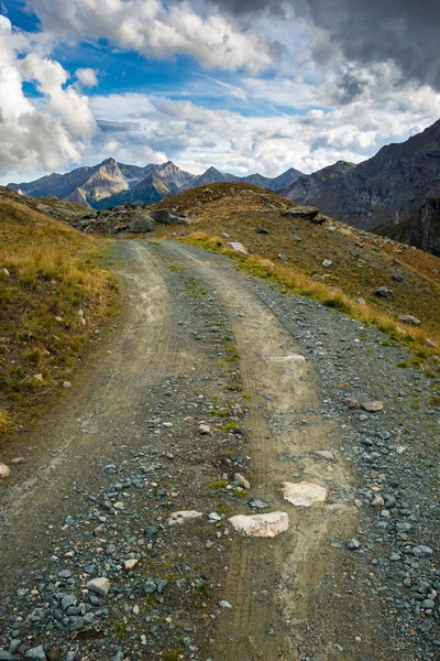 Брудна дорога в мальовничому альпійському пейзажі та драматичному небі — стокове фото
