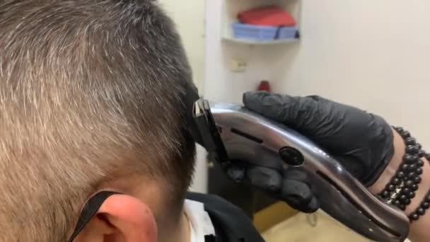 Un coiffeur portant des gants jetables noirs coupe les cheveux avec tondeuse à masqué — Video