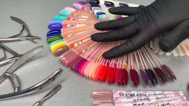 Mão do mestre em luva descartável preto passa por amostras de esmalte — Vídeo de Stock