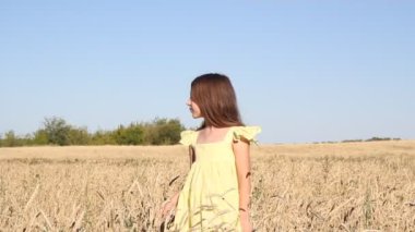 Sarı saçlı, sarı elbiseli bir kız buğday tarlasında yürüyor.