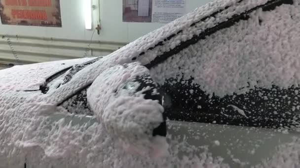 Waschen eines silberfarbenen Autos in einer Waschanlage. Das Auto ist mit weißem Schaumstoff überzogen — Stockvideo