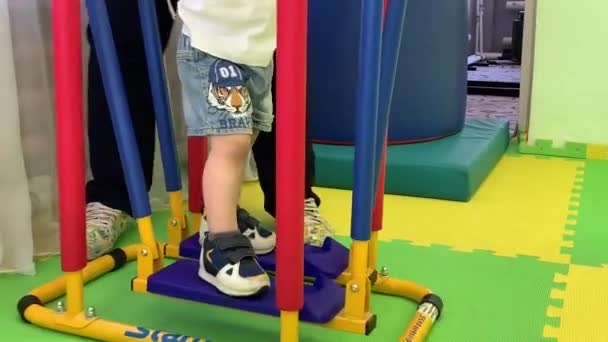 Dziecięce nóżki w niebieskich trampkach poruszają się na specjalnym symulatorze, aby przywrócić zdrowie — Wideo stockowe