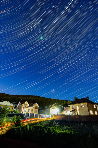 Yazın dağ köyünün yukarısındaki gece gökyüzünde yıldız izleri. Yüksek kalite fotoğraf