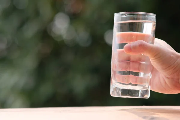 water in glass jar and hands with a bottle on a wooden background