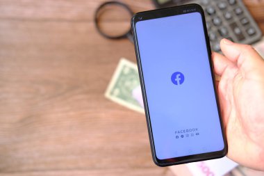 hand holding smartphone with money on wooden background 