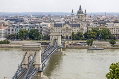 BUDAPEST, HUNGARY, 21 Temmuz 2024 - Tuna Nehri üzerindeki zincir köprü. Arka planda Macaristan, Budapeşte 'deki Gresham Sarayı ve St. Stephen Bazilikası var.