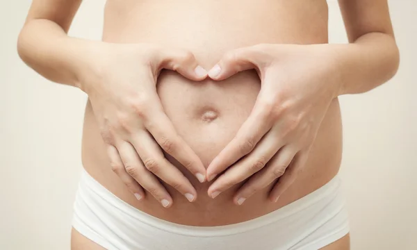 Coração em forma de mãos de mulher grávida em sua barriga — Fotografia de Stock