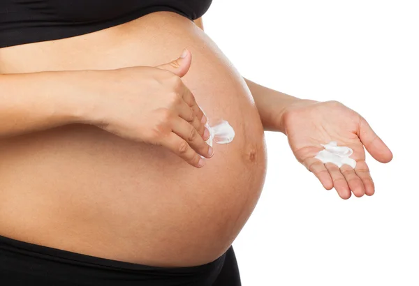 Беременная женщина массирует живот мазью против растяжки — стоковое фото
