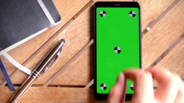 Masa tahtasında yeşil ekranlı akıllı telefon yeri, yakın plan cep telefonu krom anahtar ve işaretleyicili kahverengi masaüstte..