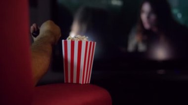 Evde kanepede film izlerken patlamış mısır yemek. Parlak ışıkları olan bir evde sahne, patlamış mısır kokulu bir film gecesi..