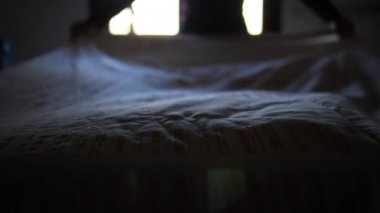 Yetişkin adam pamuklu çarşafla yatağı topluyor. Otantik modern ve gerçek hayat sahnesi.