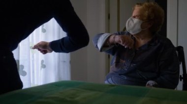 Yaşlı bir kadın ve genç bir adam, ffp2 maskesi takarken birbirlerini dirsek darbesiyle selamlıyorlar..