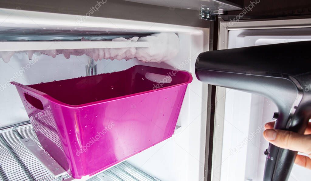 Process of defrosting ice in a home freezer. Collecting water in a plastic basin.