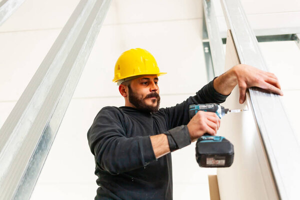 Worker screws plasterboard panels on an aluminum structure.