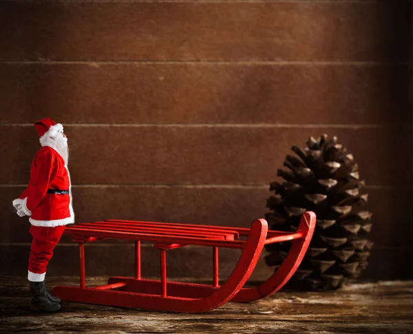 Trineo rojo con cono de pino y Santa Claus —  Fotos de Stock