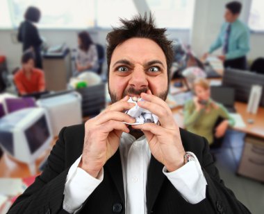 Angry businessman while eating balled paper in office. clipart