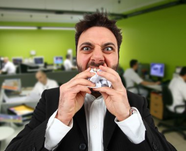 Angry businessman while eating balled paper in office. clipart