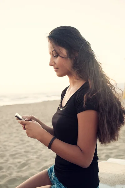 Adolescente joven mientras usa el teléfono inteligente en la playa — Foto de Stock