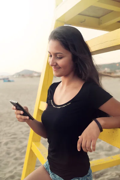 Adolescente joven mientras usa el teléfono inteligente en la playa — Foto de Stock