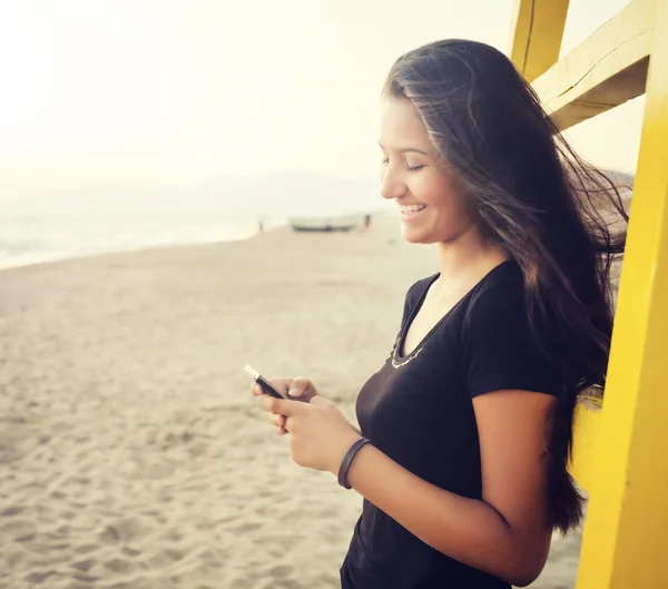 Adolescente joven mientras usa el teléfono inteligente en la playa — Foto de Stock