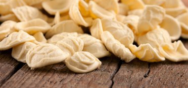 Puglia 'dan geleneksel İtalyan orkestra makarna yığını. Kulak şeklindeki şekli ile bilinir. Köy dokusunu gösterir ve yıpranmış ahşap bir masada pişirilmeyi bekler.