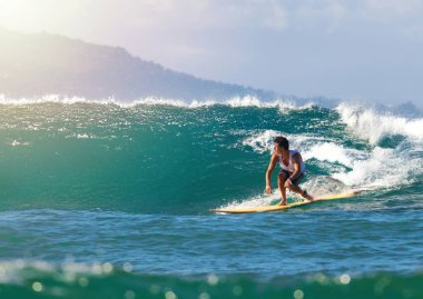 Sörf tahtasına güçlü bir okyanus dalgası oyan genç adam, yetenekli denge ve dinamik hareketi sergiliyor. Adrenalin dolu bir yaz macerası için tropik bir ortam.