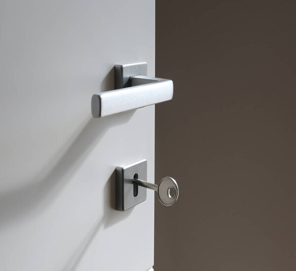 Современная стальная дверная ручка с ключом, вставленным в гладкую белую внутреннюю дверь, близко к транспортной безопасности, доступ, конфиденциальность и современный дизайн входа в дом