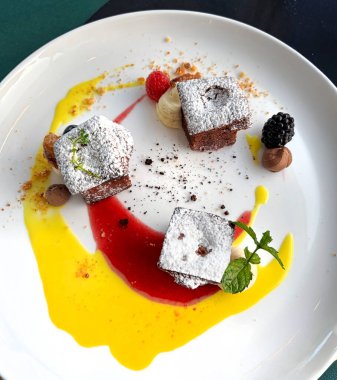 Pudra şekeri, taze ahududu ve böğürtlen ile kaplanmış gurme çikolatalı Caprese kek kareleri, zarif, hoşgörülü bir tatlı için nane ve canlı meyve püresi.