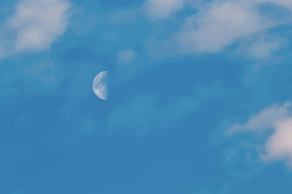 Hilal mavi gökyüzünde, gün batımında yüksek bulutlu. Bulutların olduğu yarım ay evresi. Gökteki ayın düşük açılı görüntüsü.