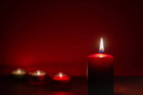 Red candle burning in dark with focus on single candle in foreground. Candlelight in dark environment and other candles in distant. Selective focus