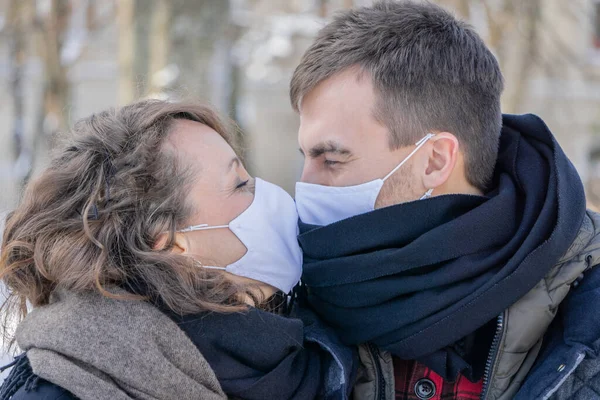 Dışarıda maskeli bir çift öpüşüyor. Erkek ve kadın dışarıda yüz maskelerinden öpüşürler. Koruyucu tıbbi maskeli sevimli çift birbirlerine bakıyorlar..