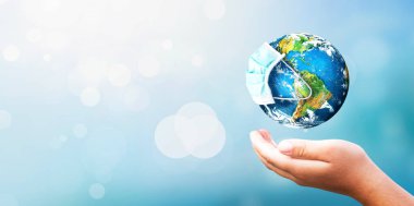 Dünya, doğanın bulanık arka planında koruma maskesi takıyor. Bu görüntünün elementleri NASA tarafından döşenmiş.. 