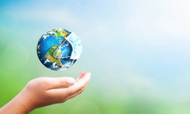 Dünya, doğanın bulanık arka planında koruma maskesi takıyor. Bu görüntünün elementleri NASA tarafından döşenmiş.. 