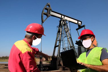 Petrol sahasında çalışan yüz maskesi kullanan ve Coronavirus COVID-19 salgını sırasında sosyal mesafeler belirleyen iki petrol işçisi. Koruyucu çalışma ortamı kavramı ve koronavirüs yayılmasını durdurun.