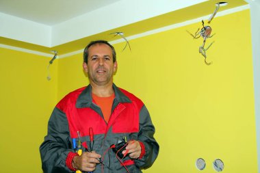 Tulum giymiş, elektrikli aletlerle gülümseyen elektrikçi, yeni bir dairede çalışıyor.