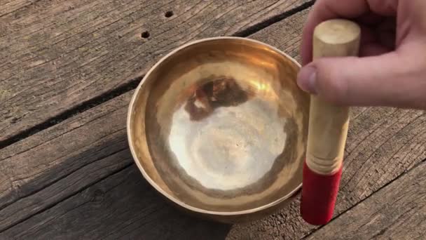 Человек играет биту на медной тибетской чаше для пения — стоковое видео