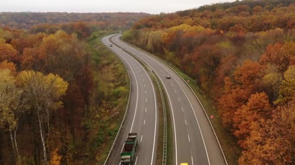 Volando a lo largo de la autopista con coches y camiones conduciendo uno hacia el otro entre árboles amarillentos — Vídeos de Stock