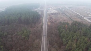 Sisli bir havada, ormanın içinde araba trafiğine doğru banliyö otobanının üzerinden uçuyor.
