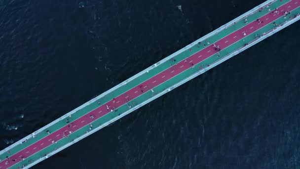 De beweging van mensen op een voetgangersbrug over een grote rivier met donkerblauw water - top down shot — Stockvideo