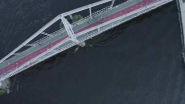 İnsanlar nehir kıyısındaki yaya köprüsünde kumla dolu bir kargo mavnası ile yürüyorlar.