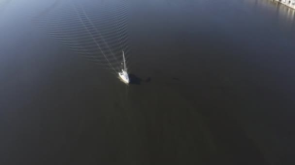 Mavi derin sularda küçük beyaz bir yat yüzüyor. Dron yörüngesinde dönüyor. — Stok video