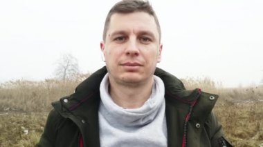 Baharda sisli bir çayırın arka planında ceketli kısa saçlı bir adam.