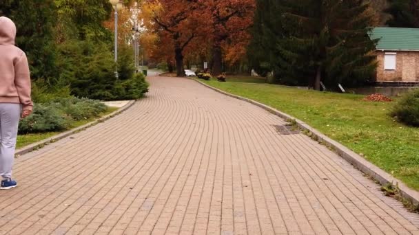 Mujer Camina a lo largo del camino de asfalto del parque a principios de otoño - Slow Motion — Vídeos de Stock
